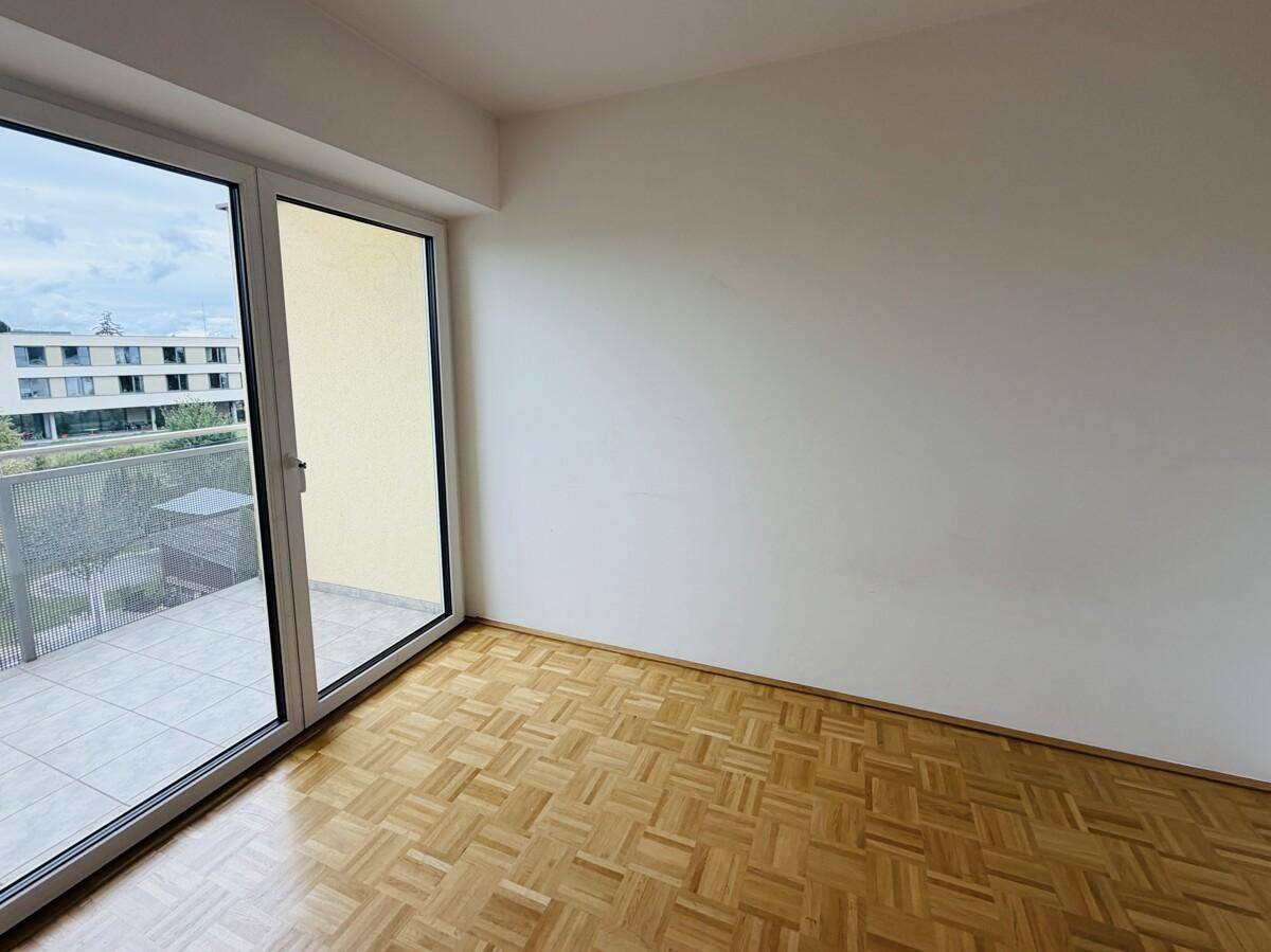 Geräumiges Zimmer mit Parkettboden und großer Schiebetür, die auf einen Balkon führt.