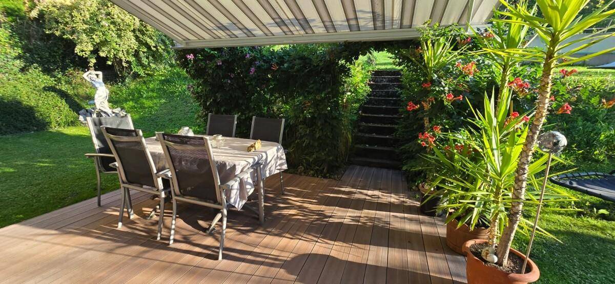 Überdachte Holzterrasse mit Esstisch und Blick auf den Garten und eine Treppe.