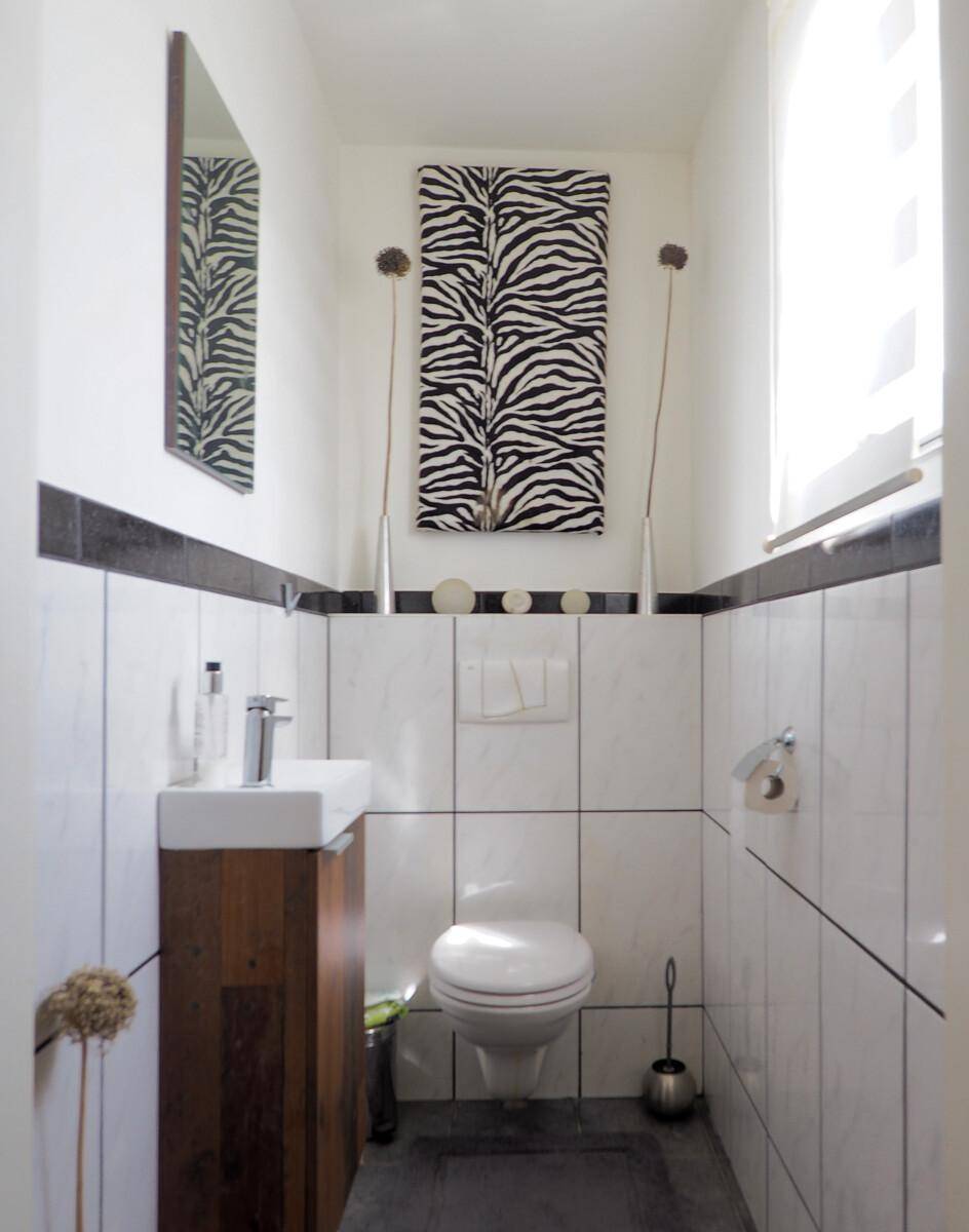 Modernes Gäste-WC mit Wand-WC, kleinem Waschbecken und dekorativer Zebra-Wandkunst.