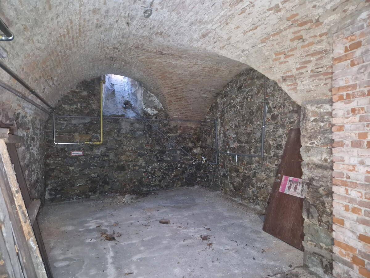 Rustikaler Kellerraum mit Gewölbedecke, unverputzten Steinwänden und Betonboden.