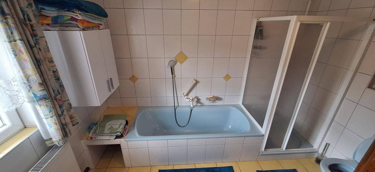 Badezimmer mit blauer Badewanne, Duschkabine und weißen Fliesen mit gelben Akzenten.