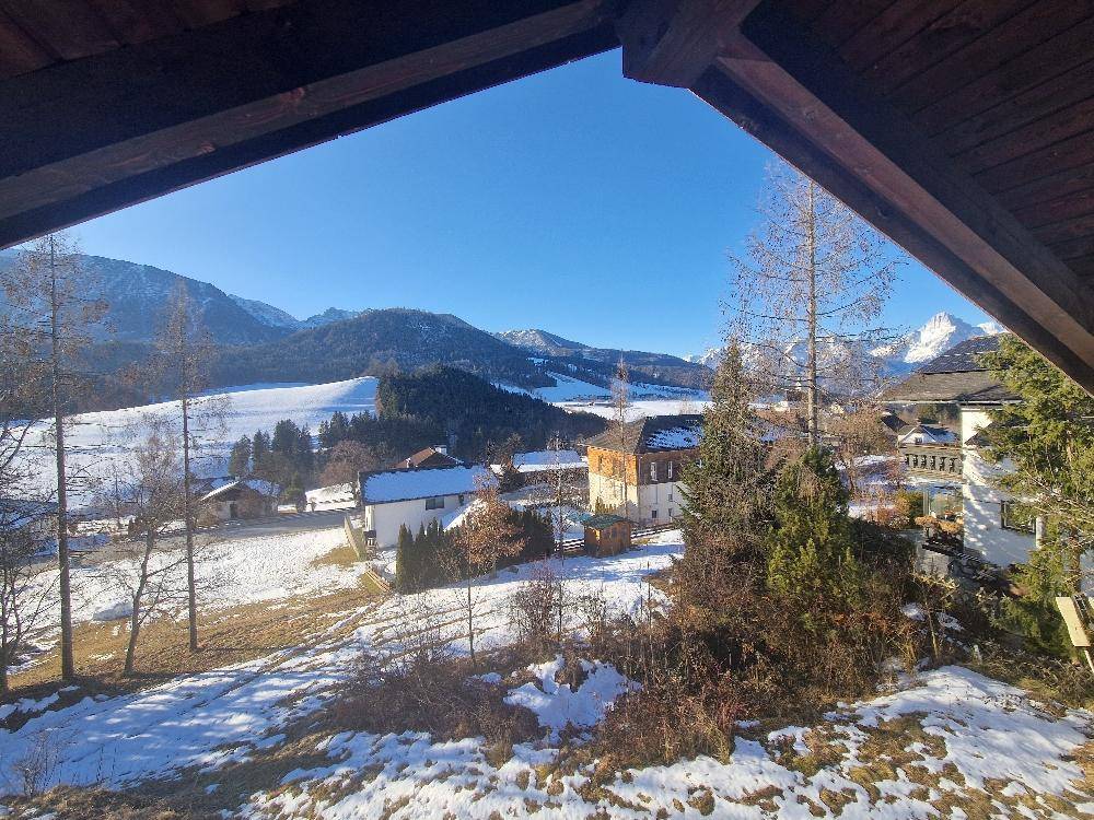 Winterliche Aussicht auf schneebedeckte Landschaft mit Häusern und Bergen unter strahlend blauem Himmel.