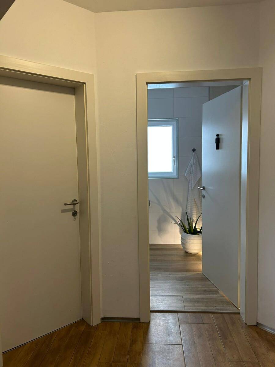 Heller Flur mit Zugang zu einem Badezimmer, ausgestattet mit Holzoptik-Fliesenboden.