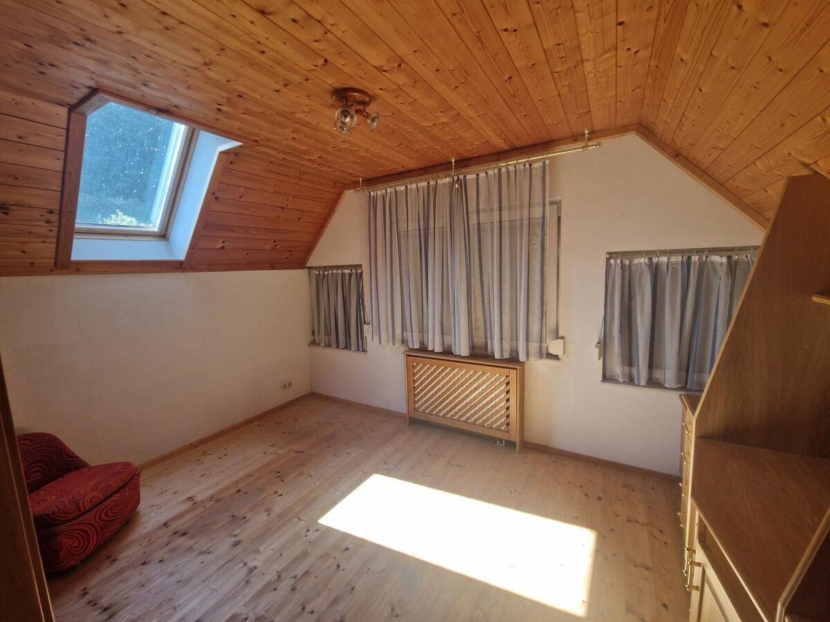 Gemütliches Dachzimmer mit Holzvertäfelung an Decke und Boden, einem Dachfenster und viel natürlichem Licht.