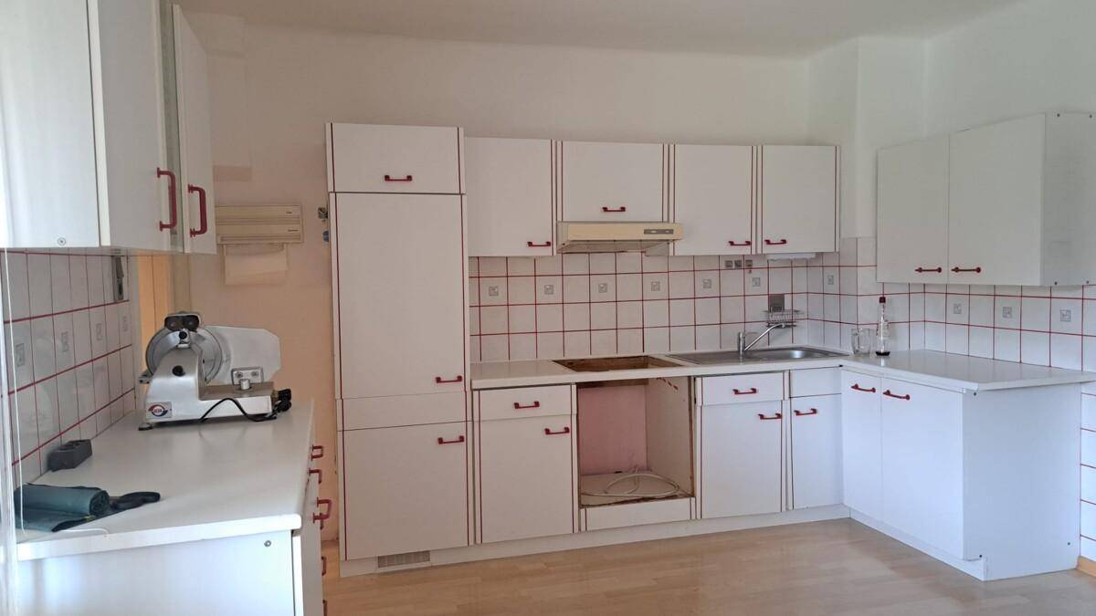 Einfache weiße Einbauküche mit roten Griffen und Fliesenspiegel, renovierungsbedürftig.