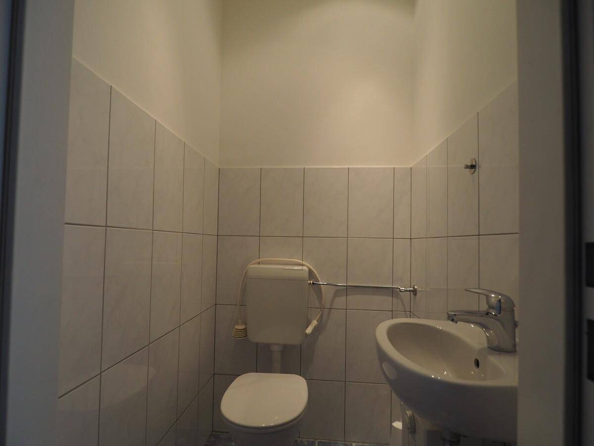 Kleiner Toilettenraum mit weißen Fliesen an den Wänden, einem Waschbecken und einer Toilette.