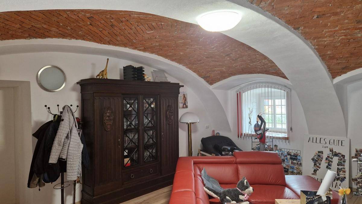 Gemütliches Wohnzimmer mit Ziegelgewölbedecke, rotem Sofa und traditionellen Möbeln, die zum Verweilen einladen.