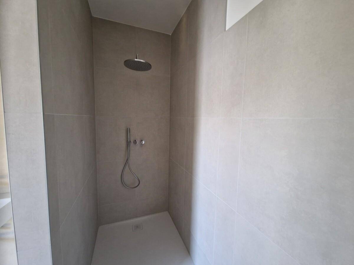 Modernes Badezimmer mit großformatigen grauen Fliesen und Regendusche.