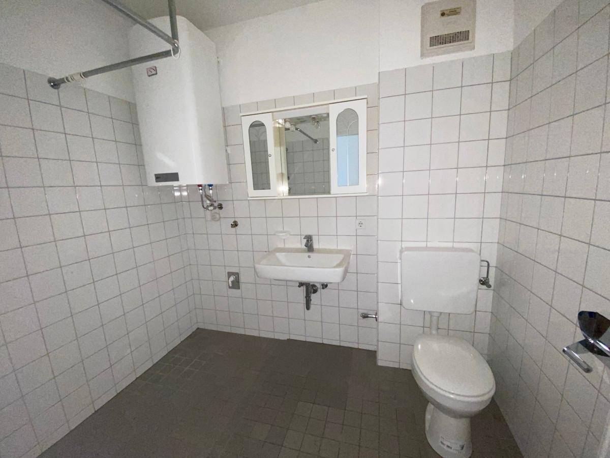 Funktionales Badezimmer mit weißen Wandfliesen, dunklem Fliesenboden, Toilette und Waschbecken.