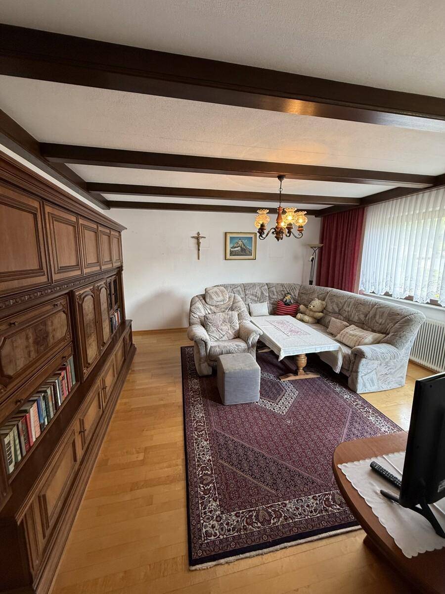 Gemütliches Wohnzimmer mit Holzbalkendecke, großem Schrank und Teppich.
