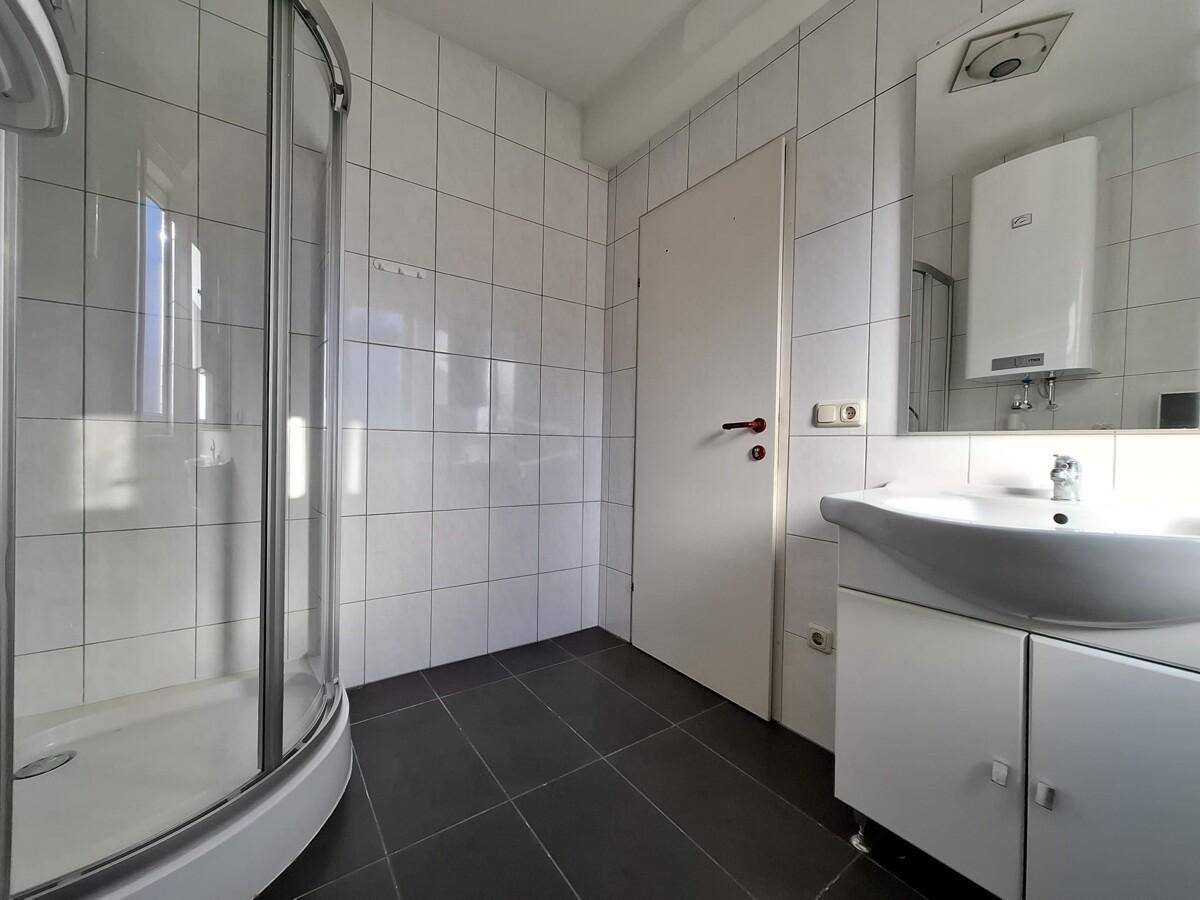 Badezimmer mit Duschkabine, Waschbecken und Spiegel, hell gefliest und funktional.
