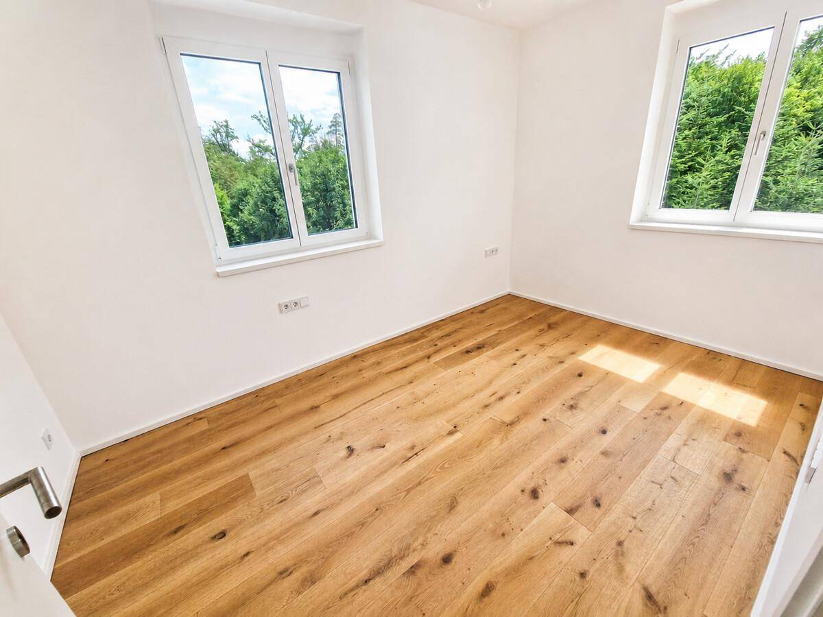 Helles Schlafzimmer mit zwei Fenstern, Holzboden und Blick ins Grüne.
