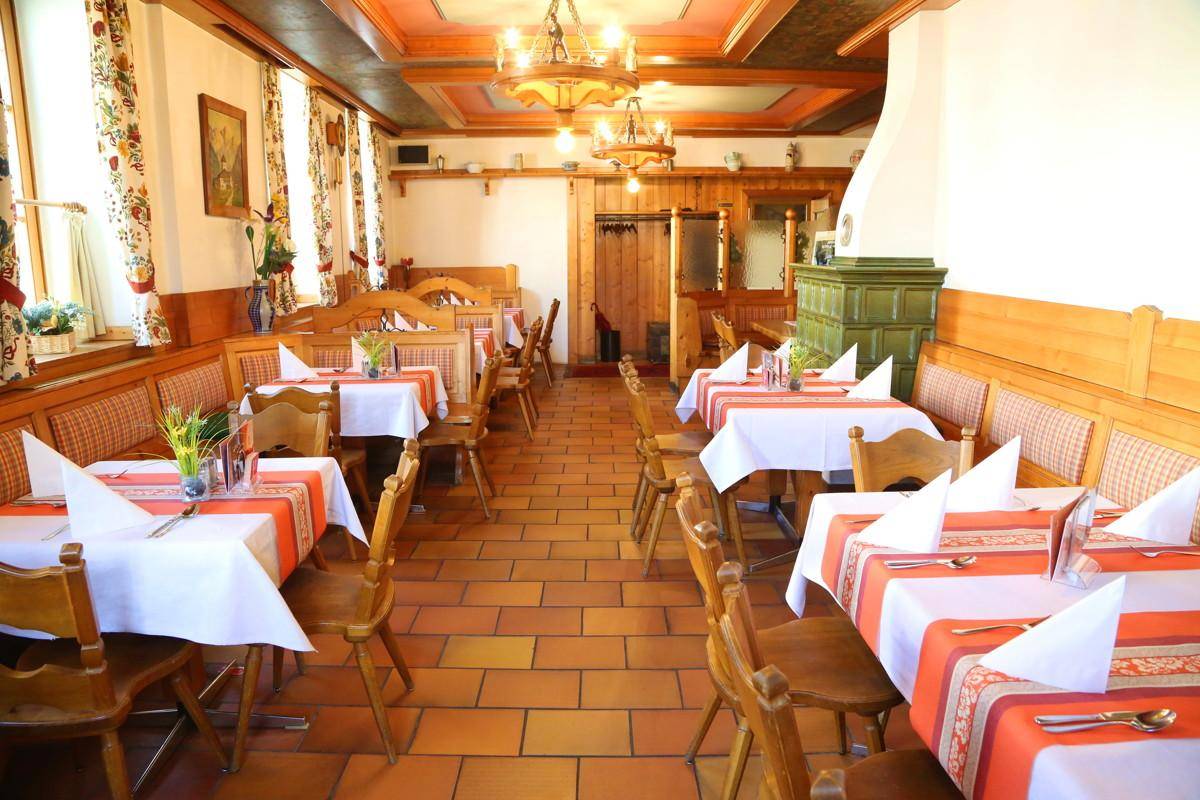 Geräumiger Speisesaal mit Holzböden, traditionellen Tischen und einem Kachelofen.