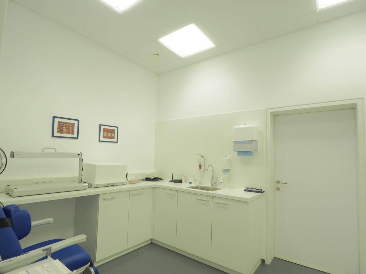 Behandlungsraum mit Waschbecken, Arbeitsfläche und medizinischen Geräten, hell beleuchtet.
