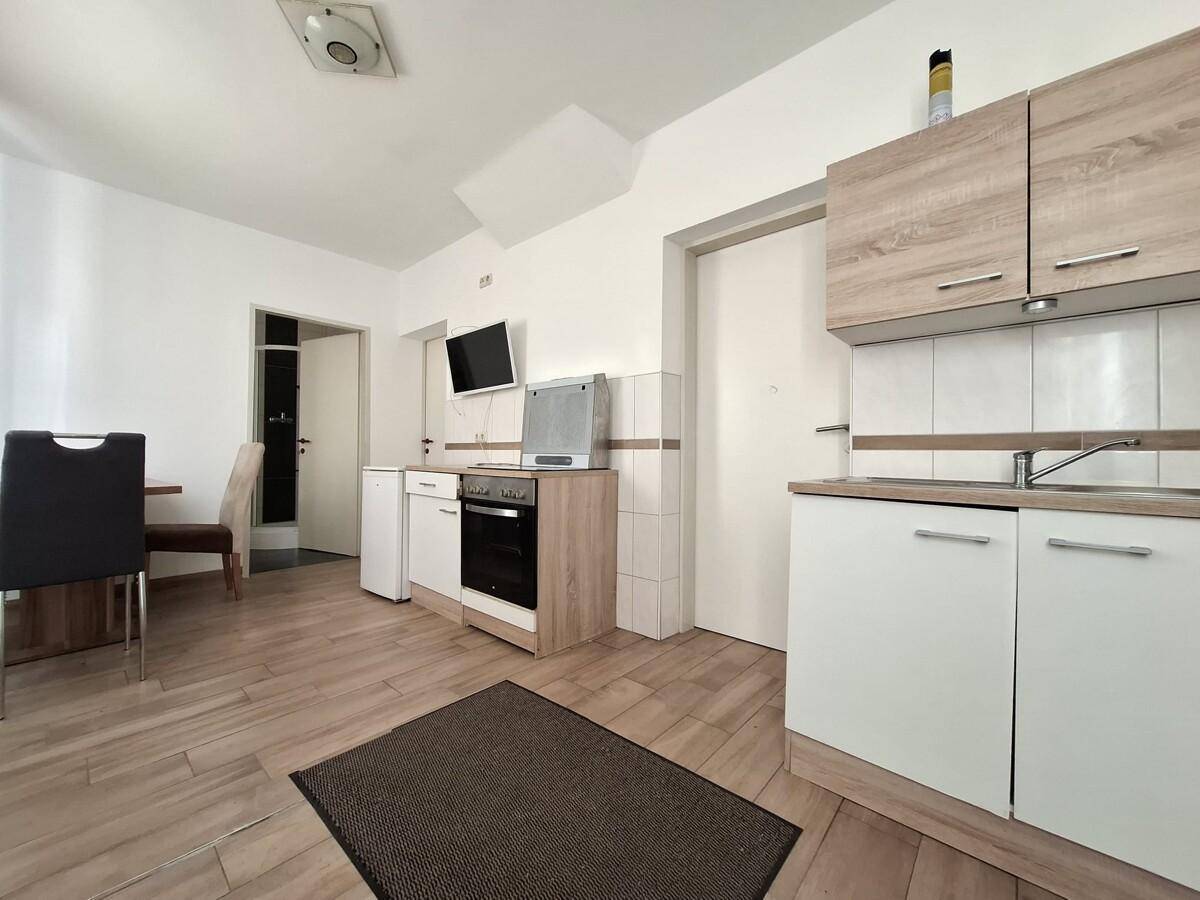 Kompakte Küchenzeile mit weißen Unterschränken, Holzoptik-Arbeitsplatte und integriertem Backofen.