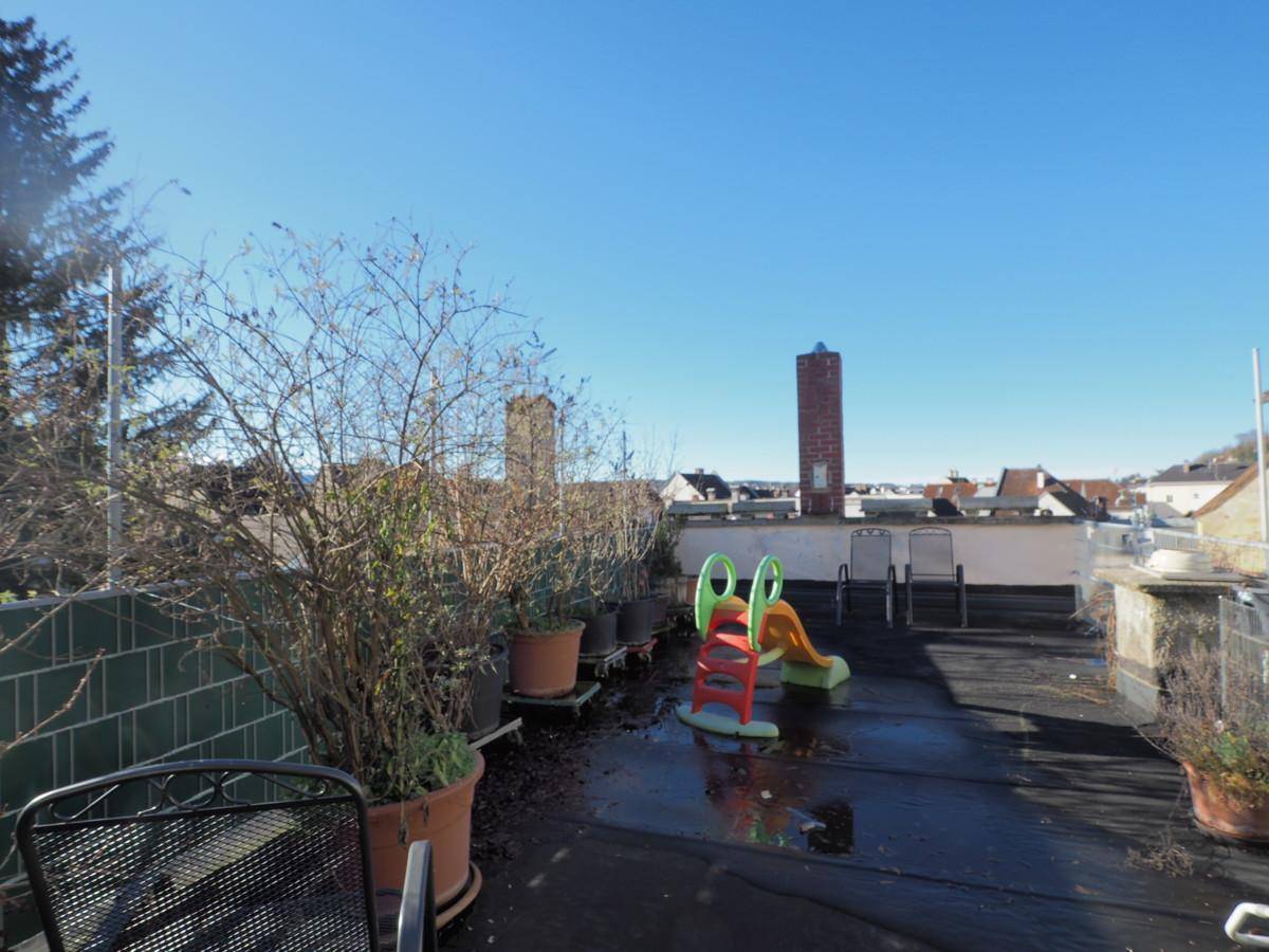 Dachterrasse mit Spielrutsche, Pflanzen in Töpfen und Blick über die Dächer der Stadt.