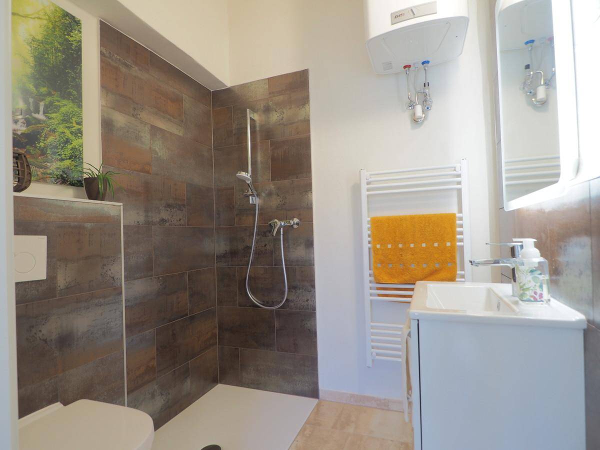 Modernes Badezimmer mit begehbarer Dusche, braunen Fliesen und weißem Waschtisch.