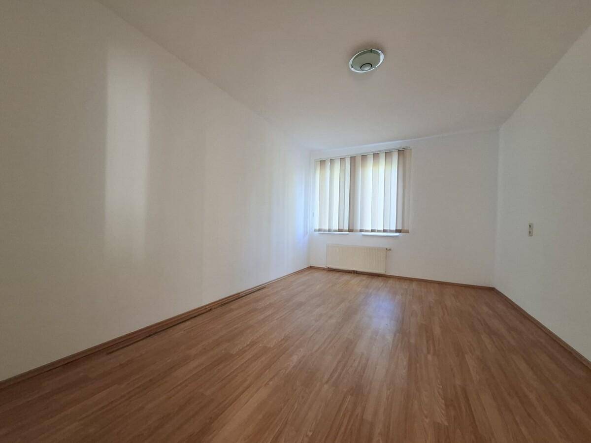 Geräumiges Schlafzimmer mit Laminatboden, weißen Wänden und einem Fenster mit Jalousien.