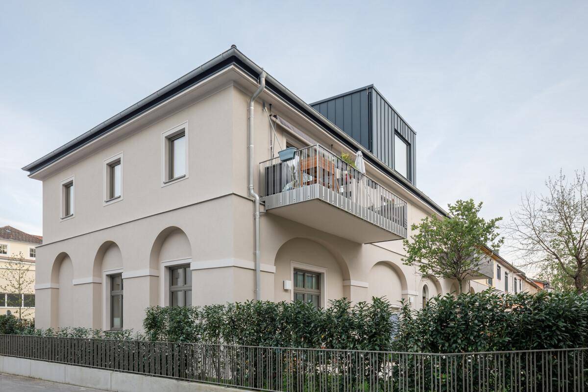 Seitenansicht eines modernen Gebäudes mit Balkon und gepflegter Hecke.