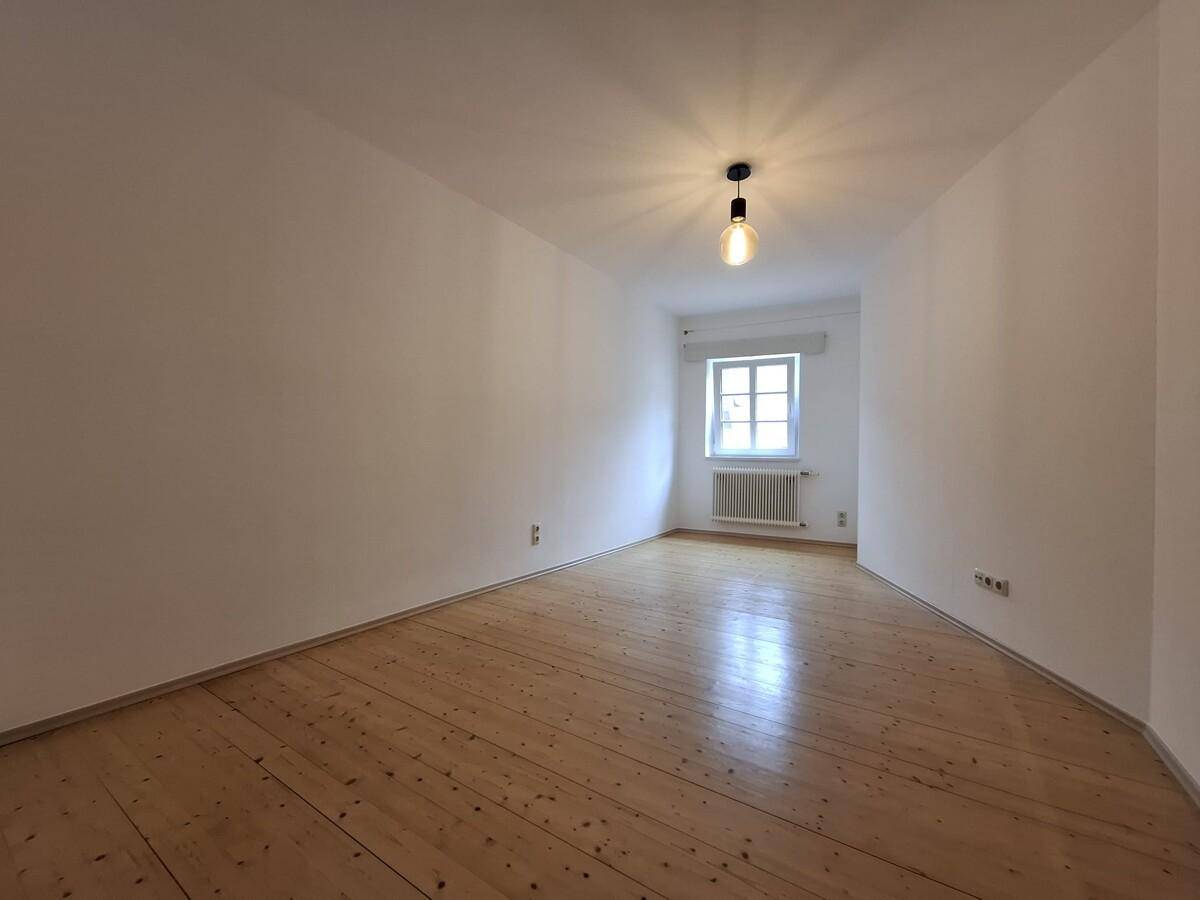 Leeres Zimmer mit hellem Holzboden, weiß gestrichenen Wänden und einem Fenster.