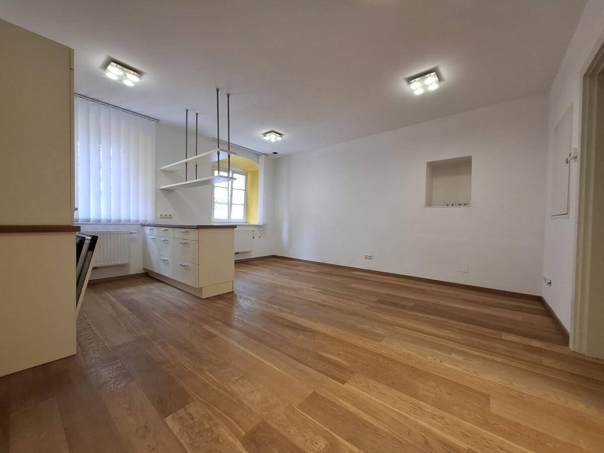 Geräumiger Wohnbereich mit Holzboden und einer Küchenzeile, die durch eine Theke abgetrennt ist.