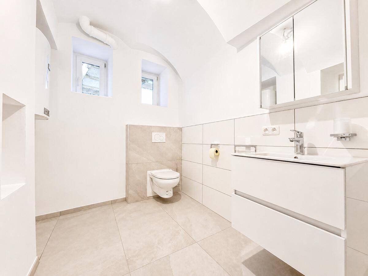 Helles Badezimmer mit wandhängendem WC, modernem Waschtisch und zwei kleinen Fenstern.
