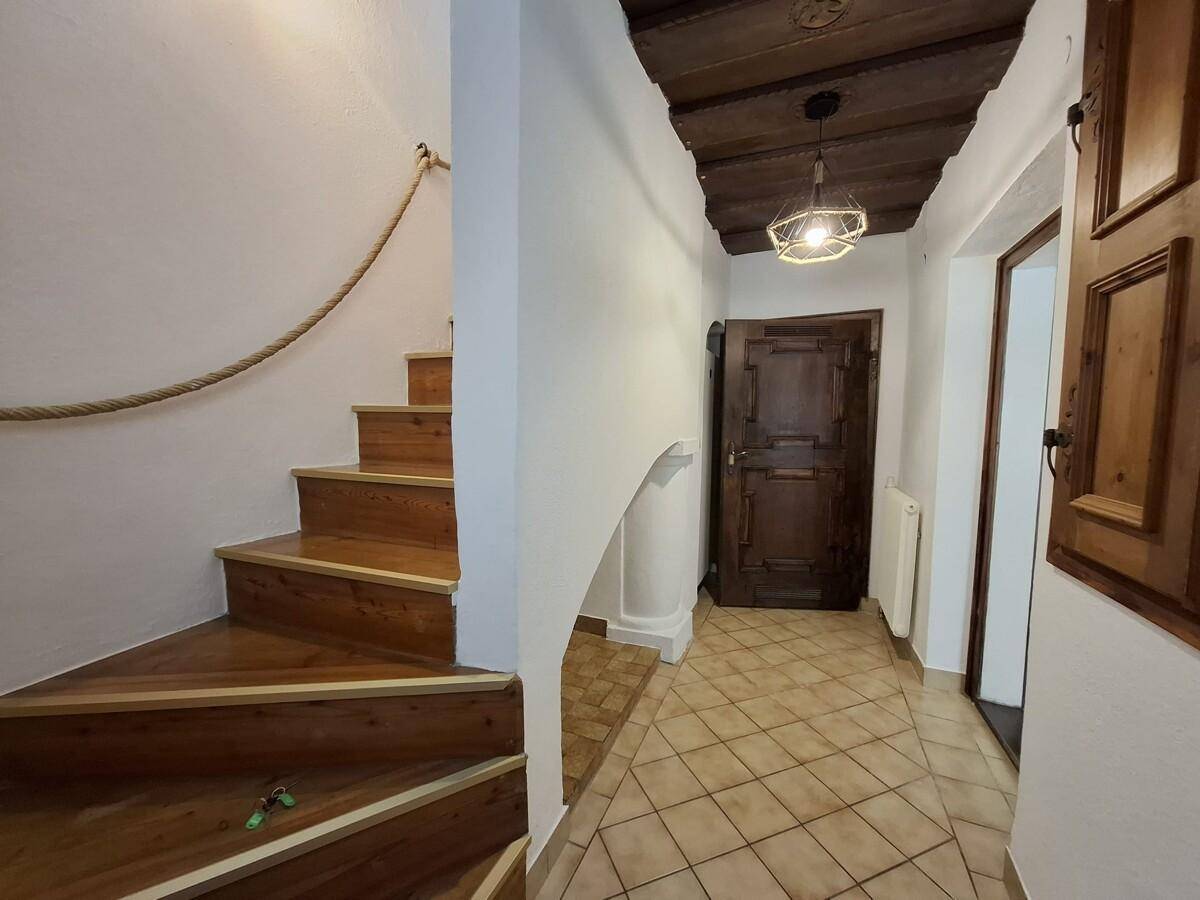 Eingangsbereich mit Holztreppe, gefliestem Boden und rustikaler Holzdecke.
