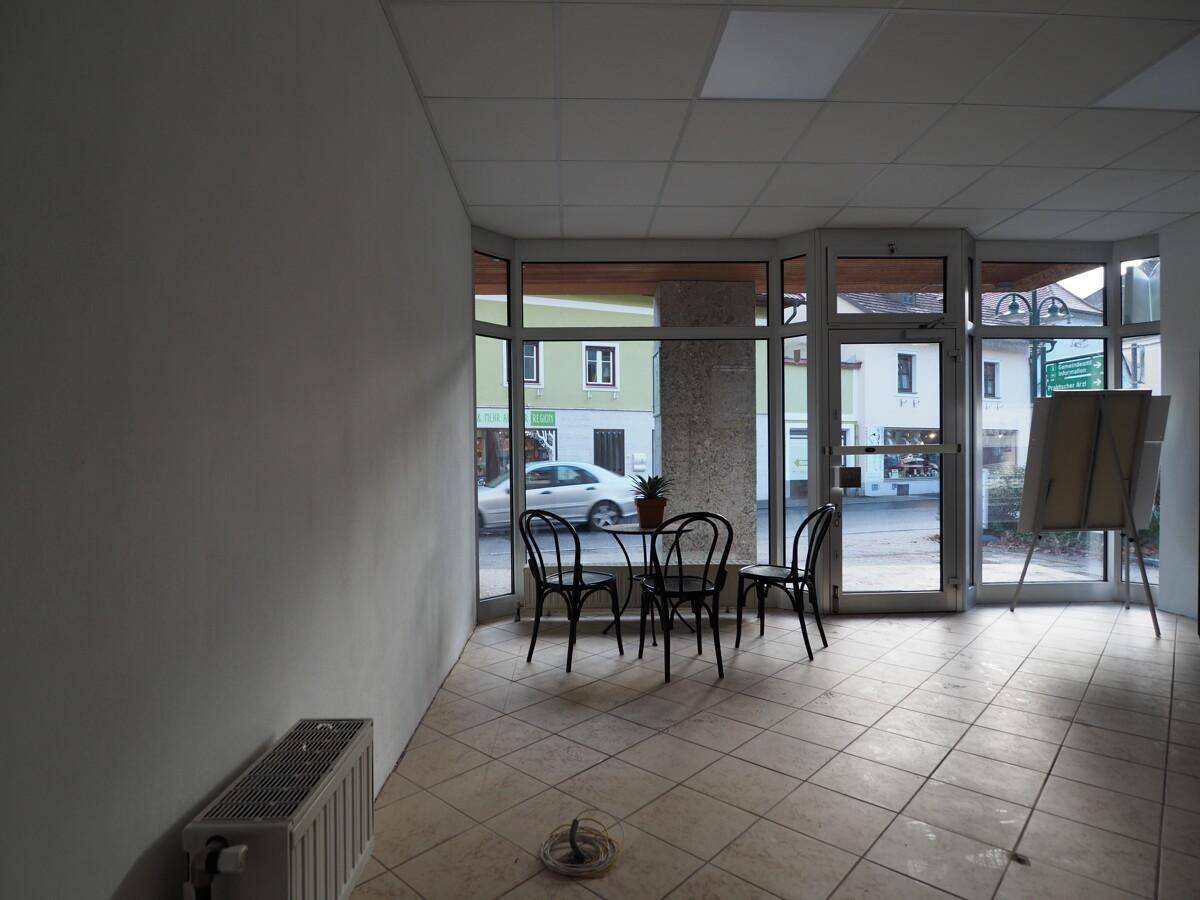 Heller Geschäftsraum im Erdgeschoss mit Fliesenboden, großen Fenstern und Blick auf die Straße.
