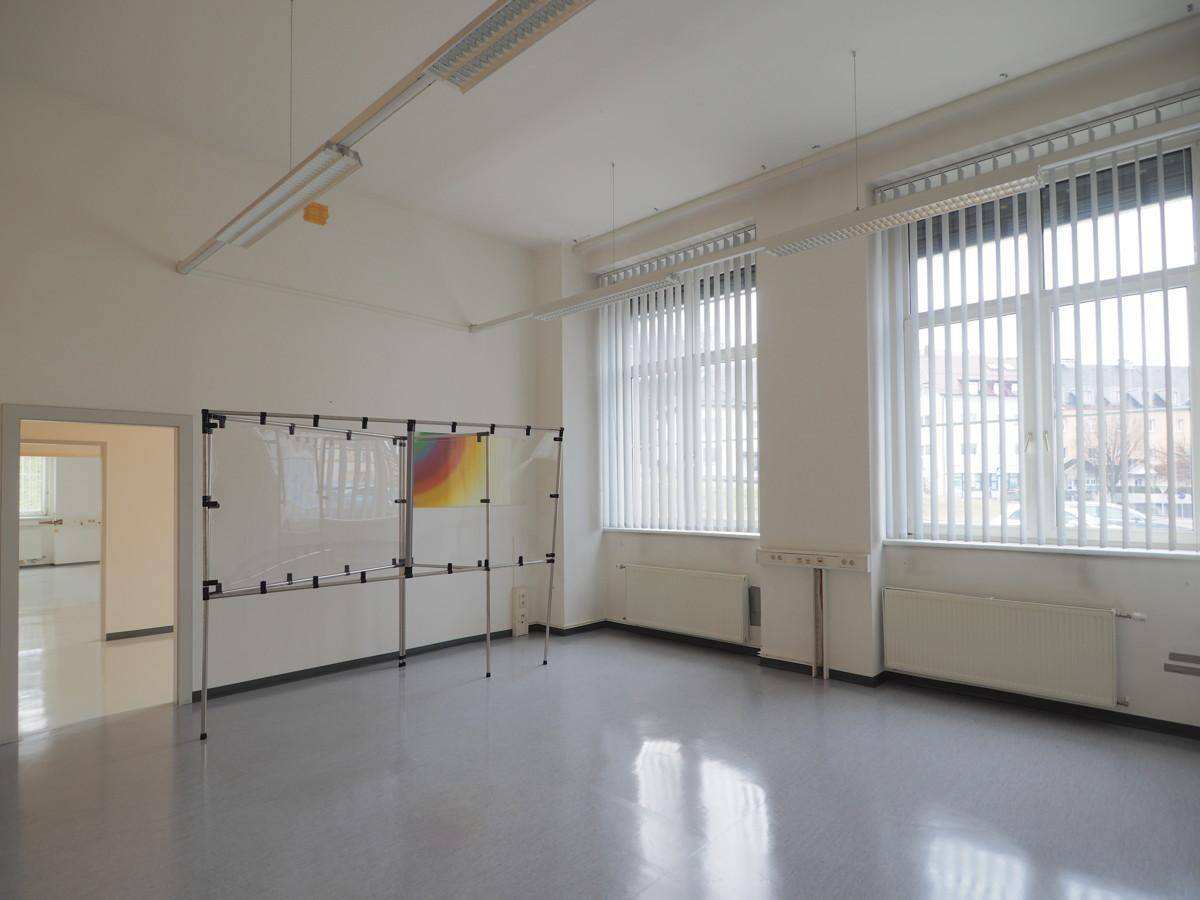 Heller Büroraum mit großen Fenstern, vertikalen Jalousien und einem flexiblen Trennsystem.