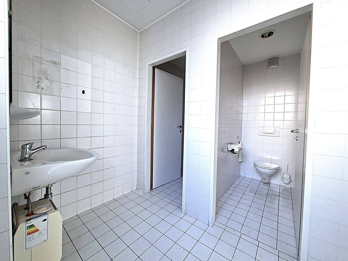 Gefliestes Badezimmer mit Waschbecken und separater Toilettenkabine, funktional und hell.