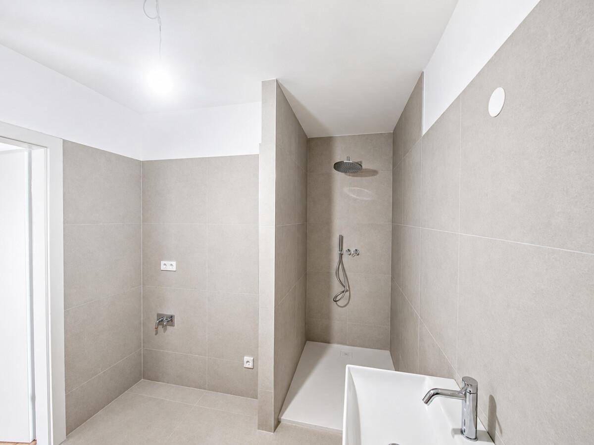 Modernes Badezimmer mit begehbarer Dusche und Waschbecken in neutralen Grautönen.