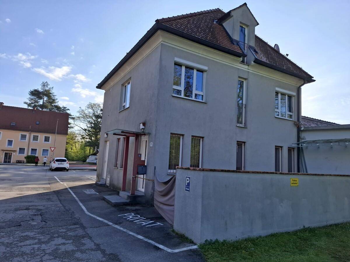 Seitenansicht des grauen Gebäudes mit Eingangsbereich und weiteren Parkmöglichkeiten.