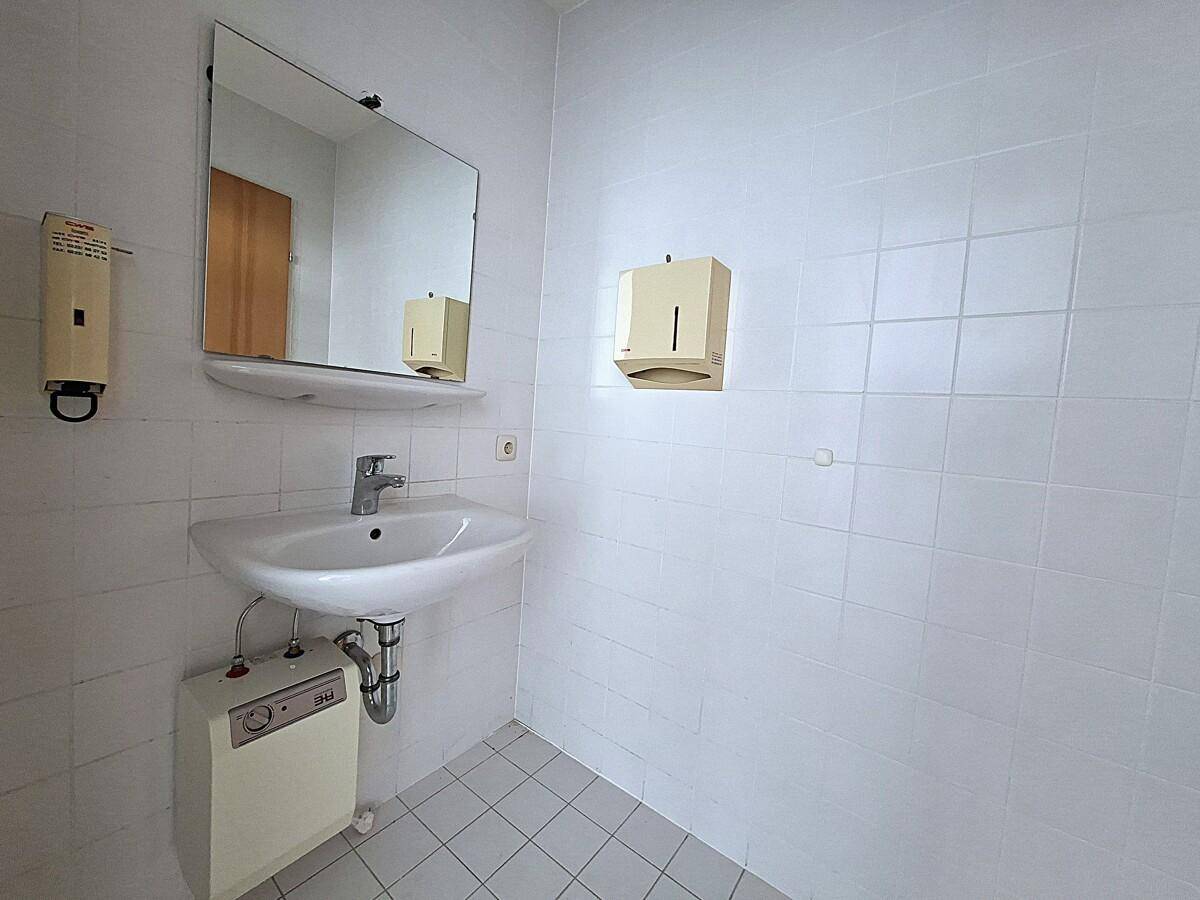 Einfaches Badezimmer mit Waschbecken, Spiegel und weißen Fliesen, funktional ausgestattet.