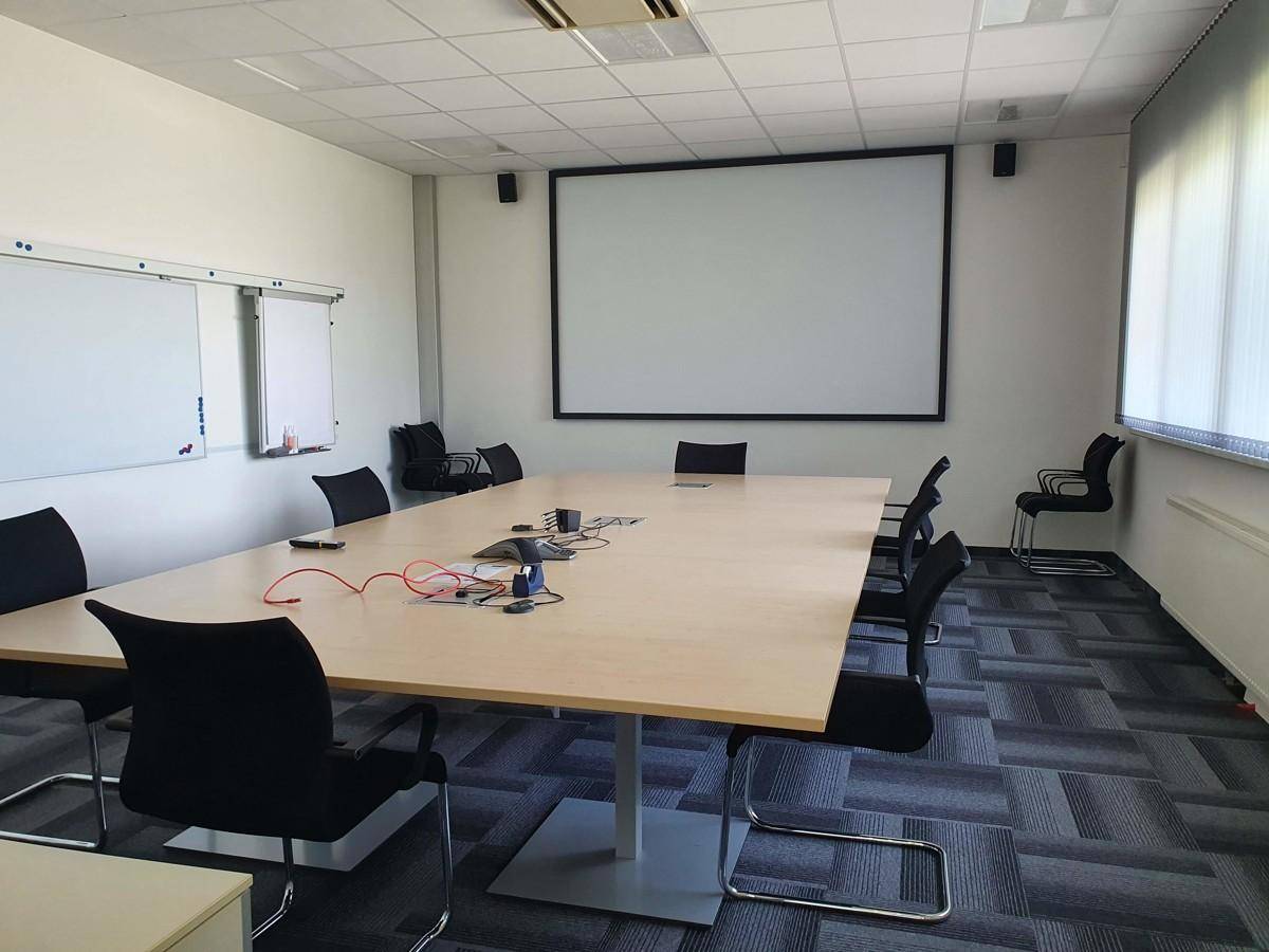 Moderner Konferenzraum mit großem Tisch, bequemen Stühlen, Projektionsleinwand und Whiteboards für Besprechungen.