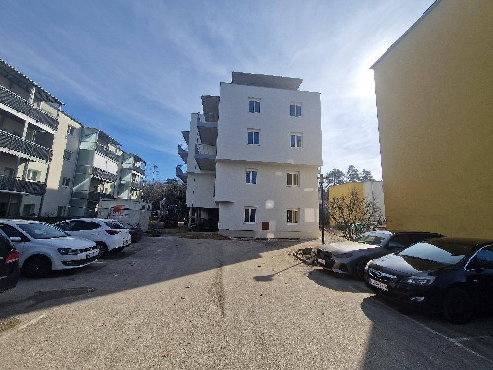 Neubau-Wohngebäude mit Parkplätzen im Vordergrund unter blauem Himmel.