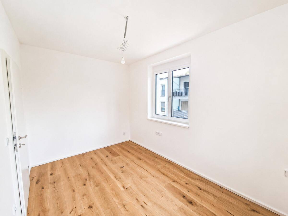 Leeres Schlafzimmer mit Holzboden und Fenster, das viel Tageslicht hereinlässt.