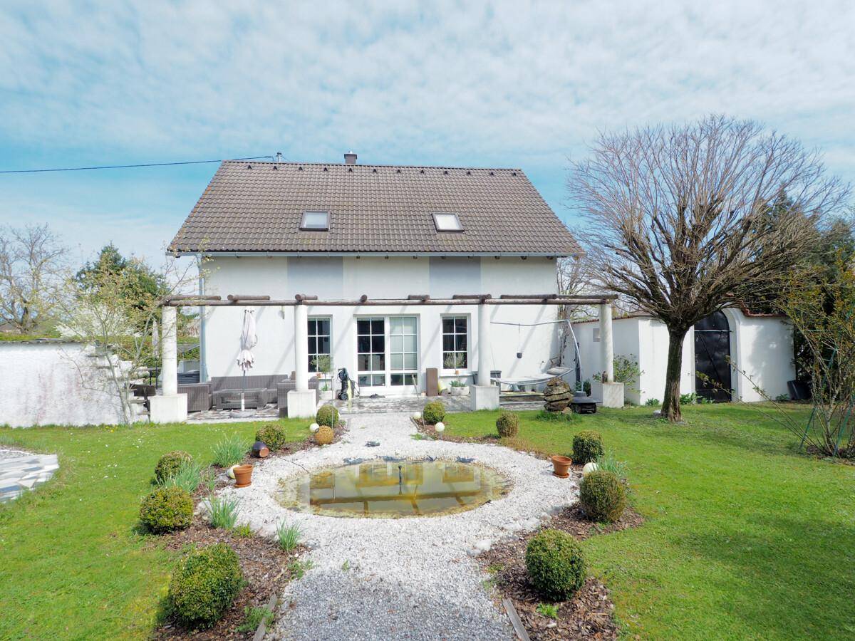 Rückansicht des Hauses mit Zugang zum Garten, Teich und einer überdachten Terrasse.