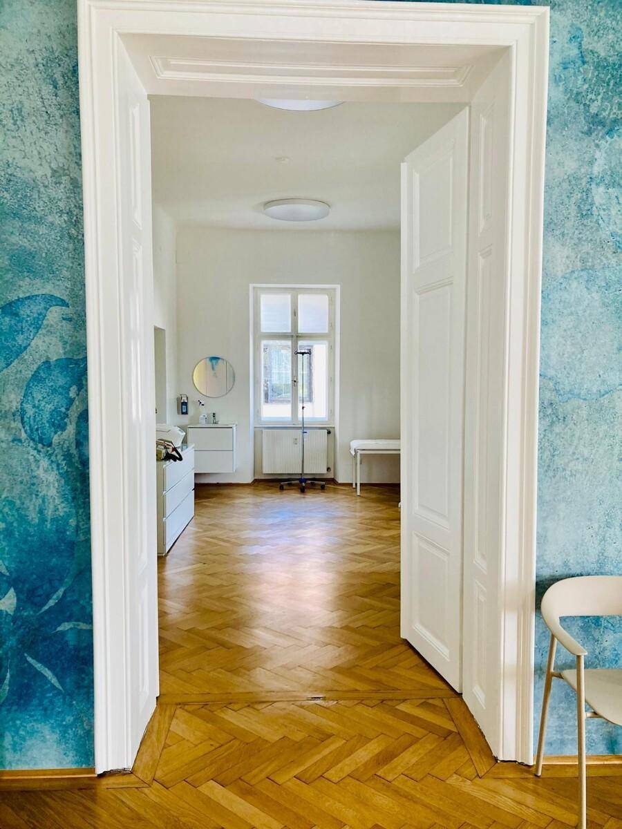 Helles Büro mit Fischgrätparkett, blauer Akzentwand und Blick ins Grüne durch das Fenster.