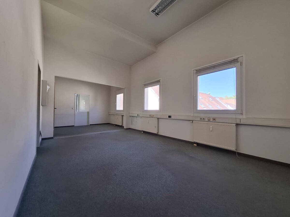 Geräumiges, leeres Büro mit Teppichboden und mehreren Fenstern, bereit zur Einrichtung.