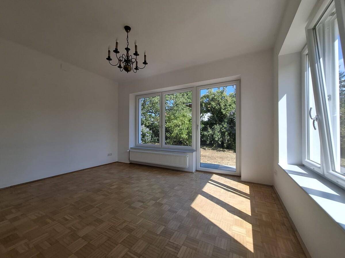 Lichtdurchfluteter Wohnbereich mit Parkettboden und großen Fenstern zum Garten.
