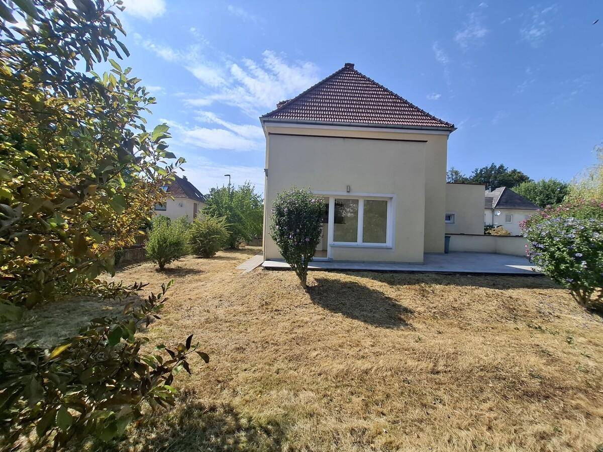 Seitenansicht des Hauses mit trockenem Rasen und Bäumen an einem sonnigen Tag.