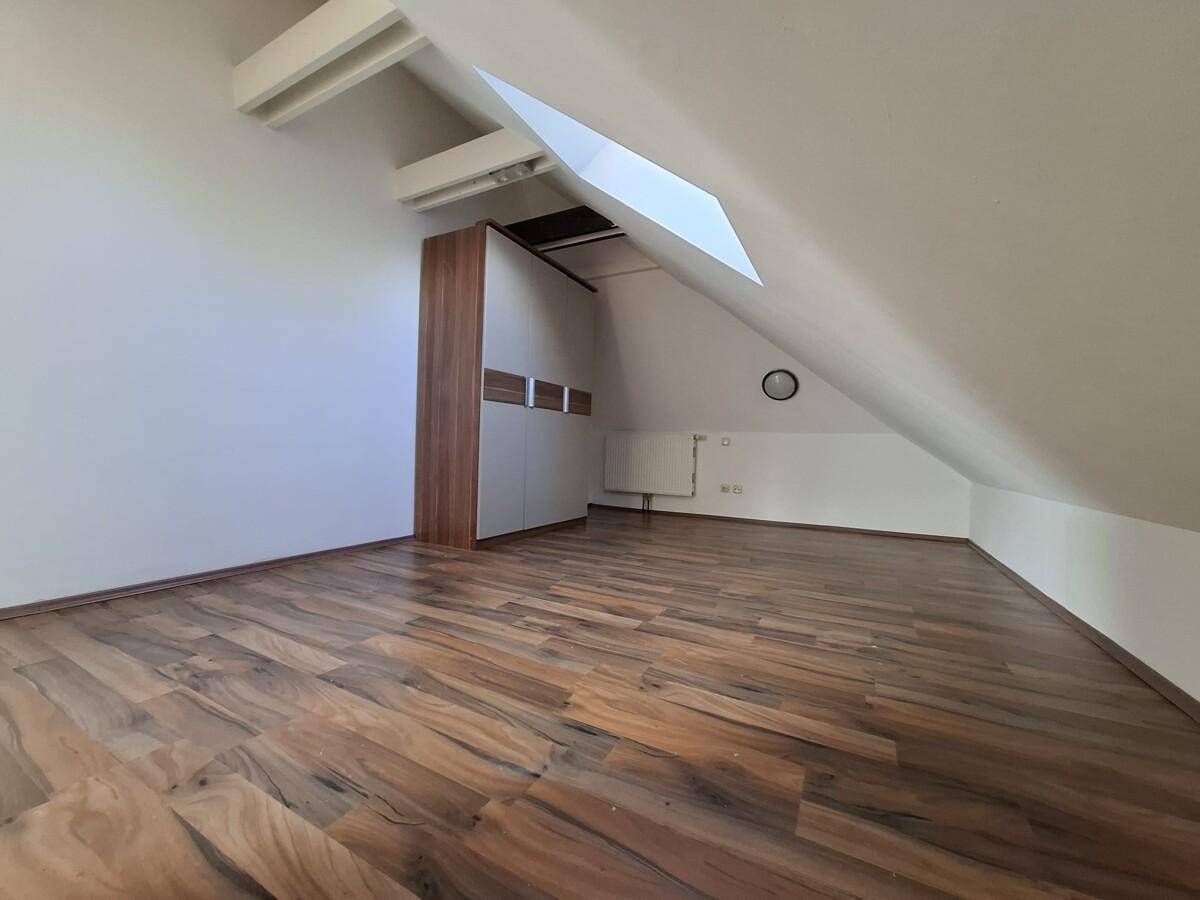 Dachgeschossraum mit Holzboden, Dachschräge, Einbauschrank und Dachfenster.