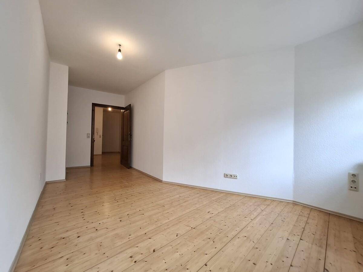 Helles Zimmer mit Holzboden und weiß gestrichenen Wänden, ideal für Schlaf- oder Arbeitsbereich.