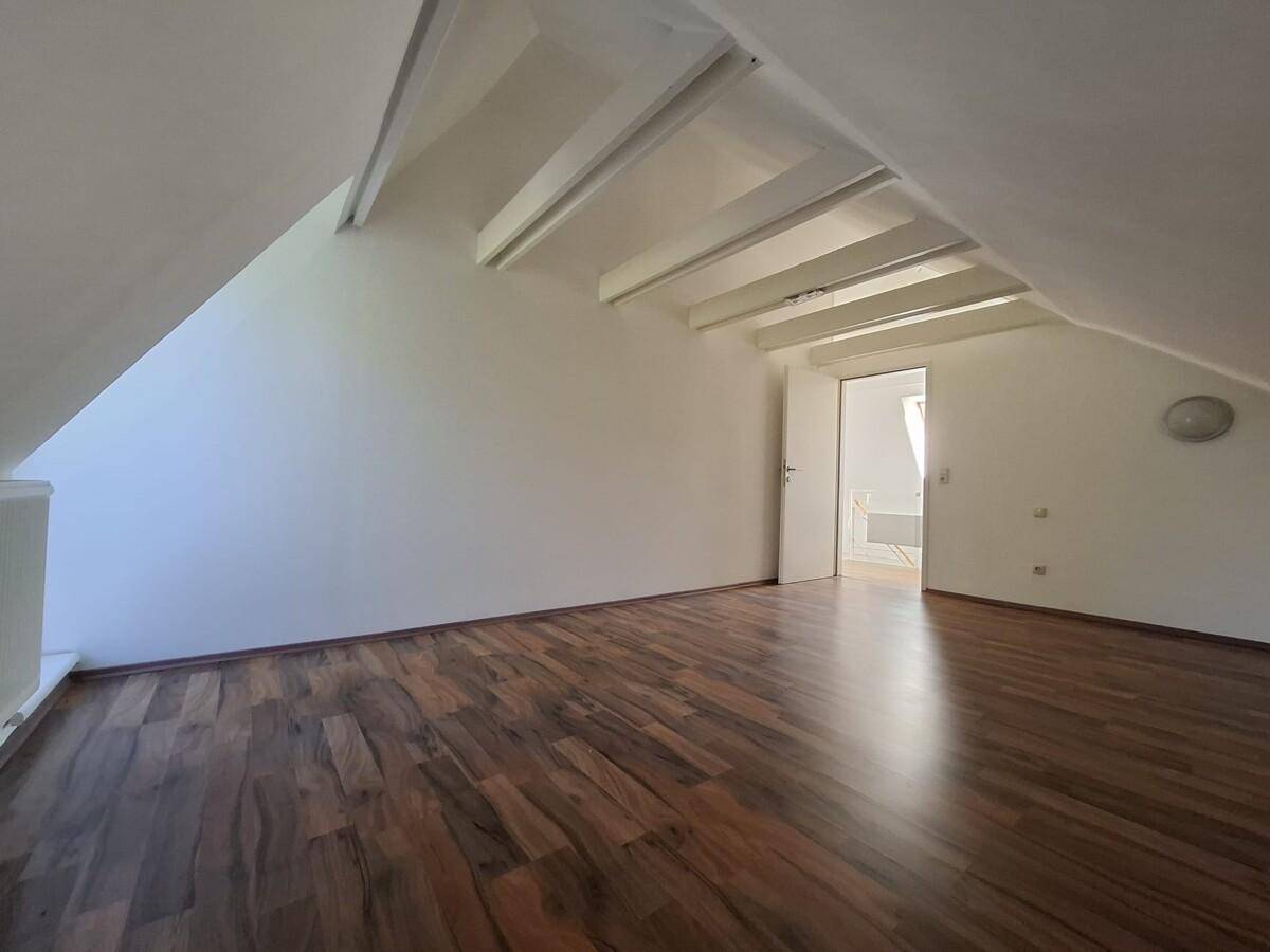 Heller Dachgeschossraum mit Holzboden, Dachschräge und Zugang zu einem weiteren Zimmer.