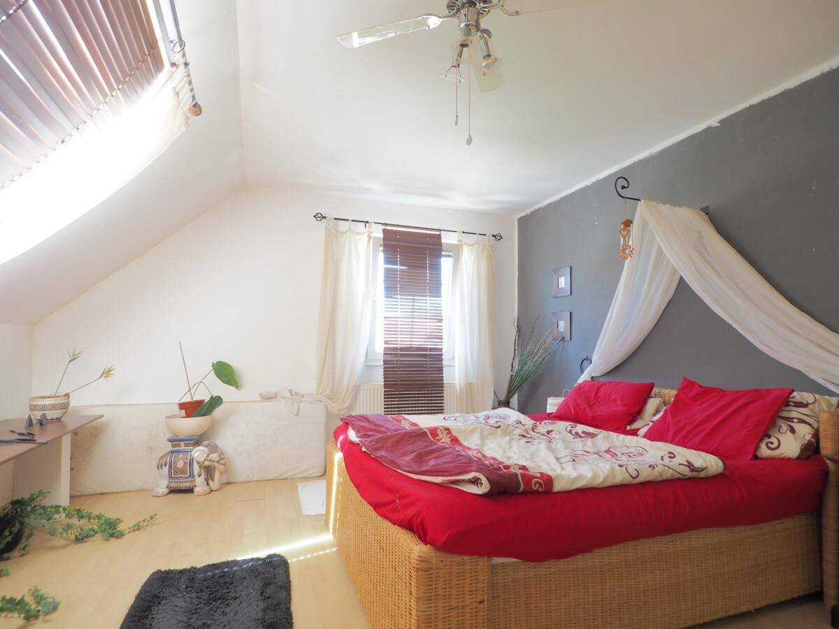 Schlafzimmer im Dachgeschoss mit schrägen Wänden, Holzboden und einem Himmelbett.