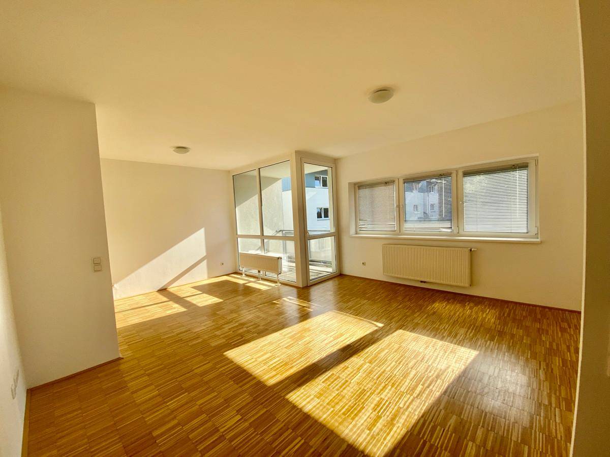 Helles Zimmer mit Parkettboden und Zugang zu einem Balkon, durchflutet von Sonnenlicht.