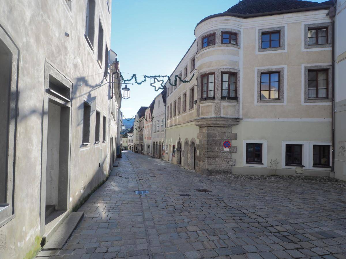 Historische Gasse mit Kopfsteinpflaster und traditionellen Gebäuden unter blauem Himmel.