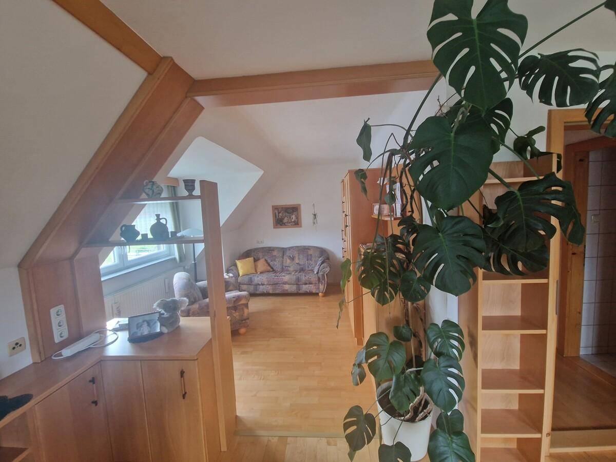 Gemütlicher Wohnbereich im Dachgeschoss mit Holzparkett, Dachschrägen und einer großen Grünpflanze.