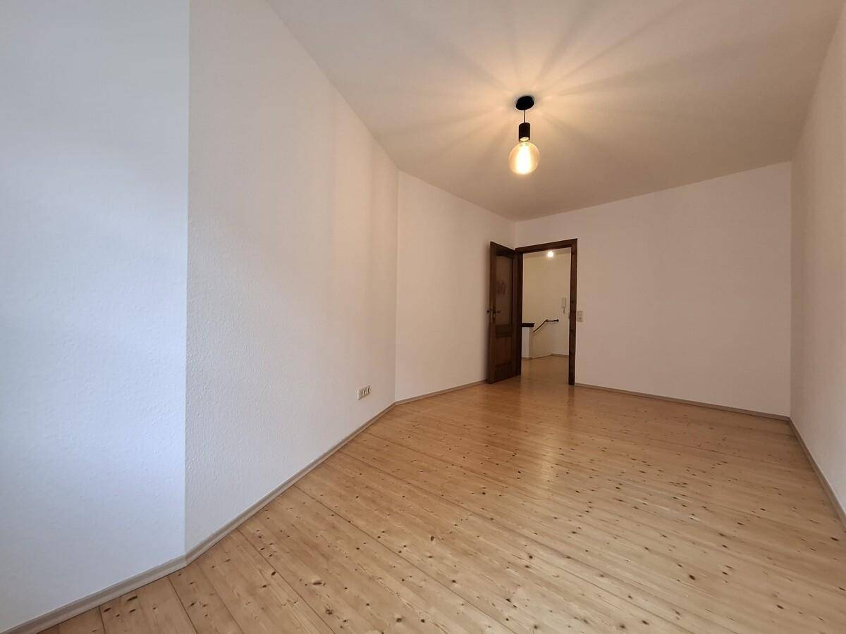 Geräumiges Zimmer mit Holzboden und einer Holztür, bereit zur individuellen Gestaltung.