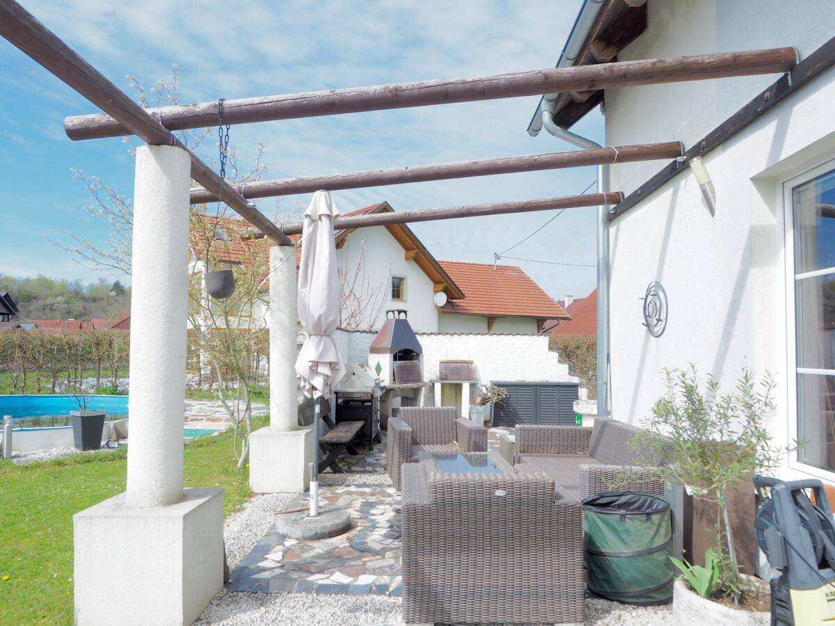 Gemütliche überdachte Terrasse mit Rattanmöbeln und Blick auf den Garten und Poolbereich.